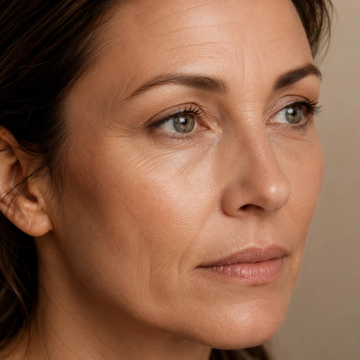 Portrait premium d’une femme entre 40 et 50 ans révélant une peau légèrement marquée par les ridules, une perte progressive d’élasticité et des traits moins fermes dans l’univers Valnay Paris