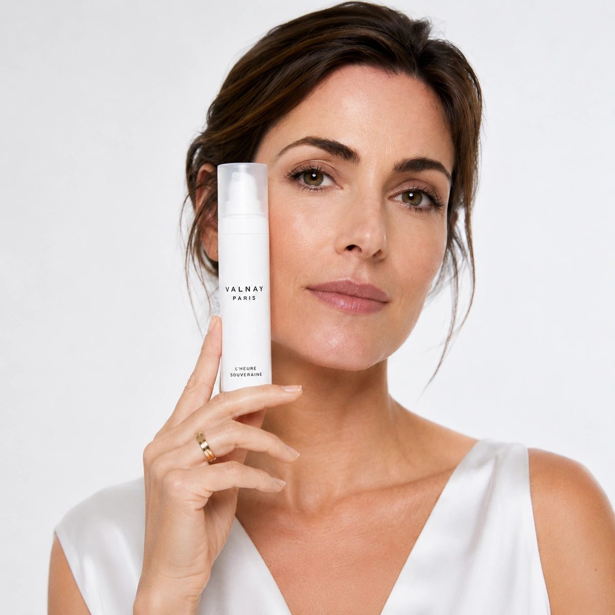 Femme tenant L'Heure Souveraine crème de jour anti-âge de Valnay Paris à côté de son visage