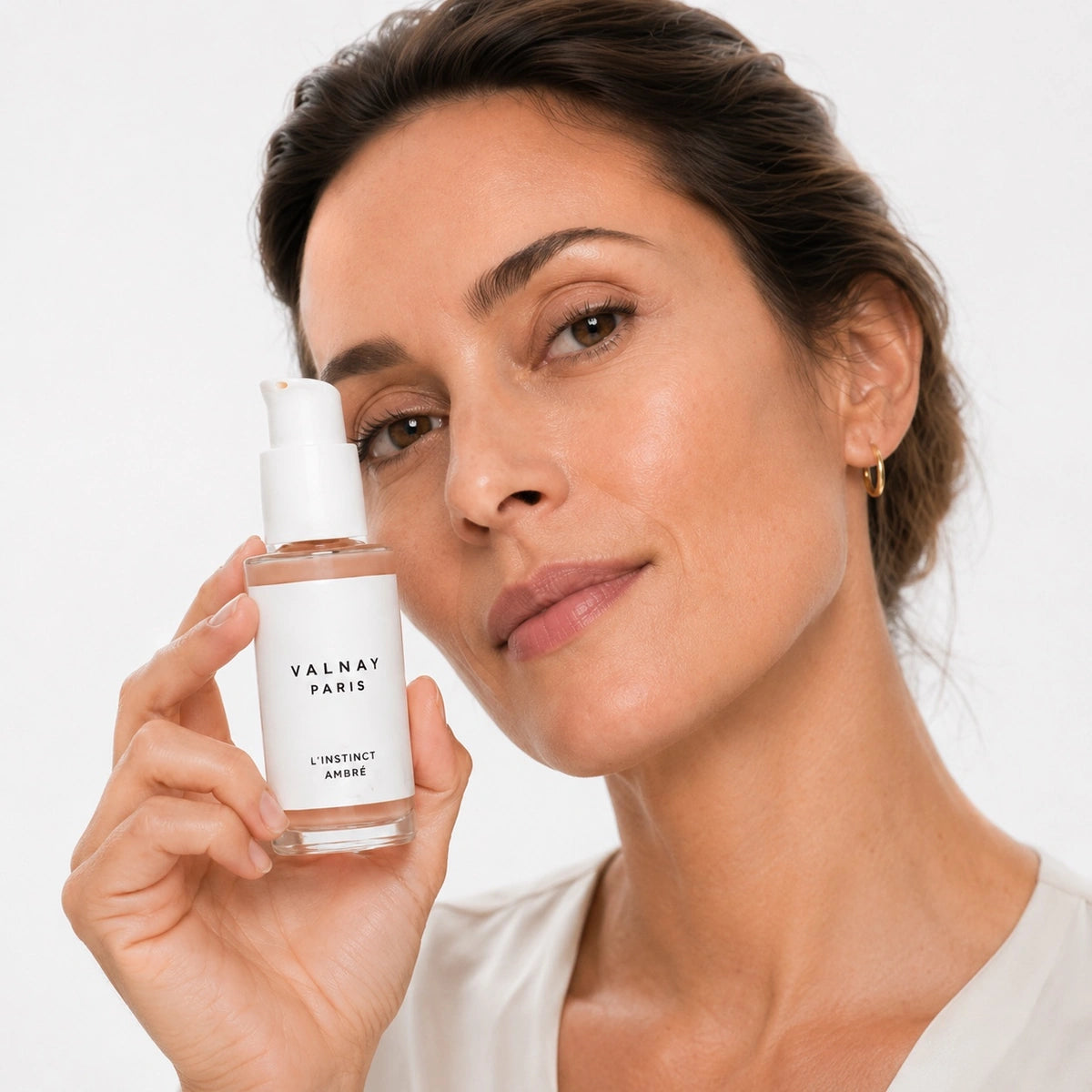 Femme tenant L'Instinct Ambré sérum anti-âge aux peptides de Valnay Paris à côté de son visage