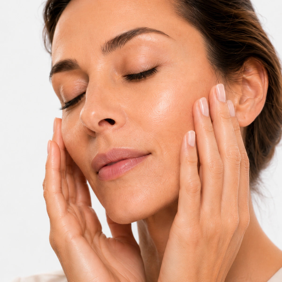 Femme à la peau lumineuse et éclatante massant délicatement son visage après l'application d'un soin anti-âge Valnay Paris