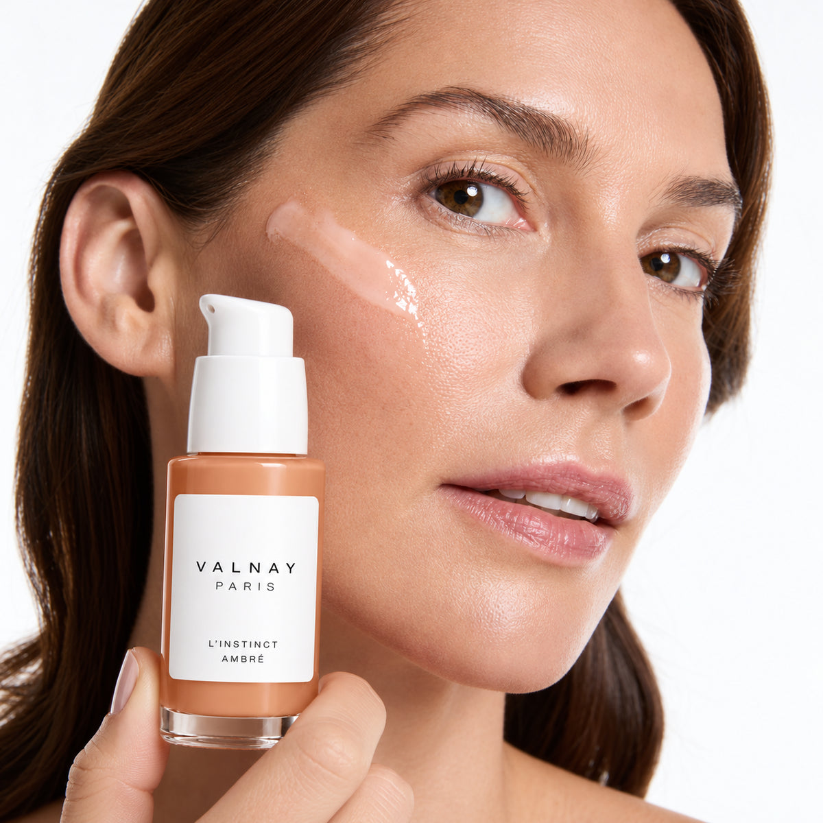 Femme tenant en main L’Instinct Ambré de Valnay, sérum anti-âge aux peptides, avec une texture de soin appliquée sur la joue pour hydrater, lisser les ridules et soutenir la fermeté de la peau